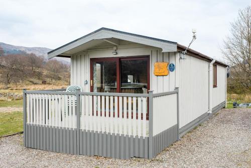 a small white shed with a porch and a fence at Lapwing Lodge with loch and mountain view in Crianlarich