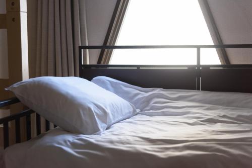 an unmade bed with a pillow in front of a window at COCOSTAY Matoba ココステイ広島駅前 in Hiroshima