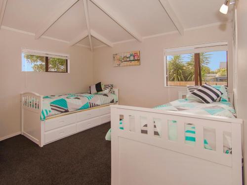 two white beds in a room with two windows at Beach Central - Whangamata Holiday Home in Whangamata