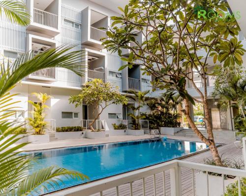 a swimming pool in front of a building with trees at The Rooms Apartment Bali by ARM Hospitality in Denpasar