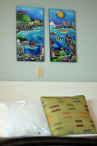 two paintings on a wall above a bed with a pillow at Anchor Inn Hotel and Suites in Twillingate