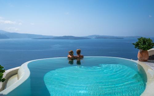 two people sitting in a swimming pool overlooking the water at Pezoules of Oia in Oia