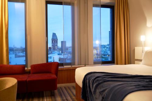 a hotel room with a bed and a chair and windows at Dorint Kurfürstendamm Berlin in Berlin