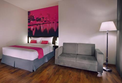 a bedroom with a bed and a chair with a painting on the wall at favehotel Graha Agung Surabaya in Surabaya