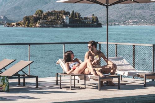 a man and a woman sitting on a bench by the water at Hotel La Palma in Stresa