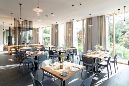 um restaurante com mesas e cadeiras de madeira e janelas grandes em Bader Hotel em Parsdorf