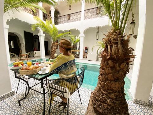 a woman sitting at a table next to a pool at Riad Fabiola Et Spa in Marrakesh
