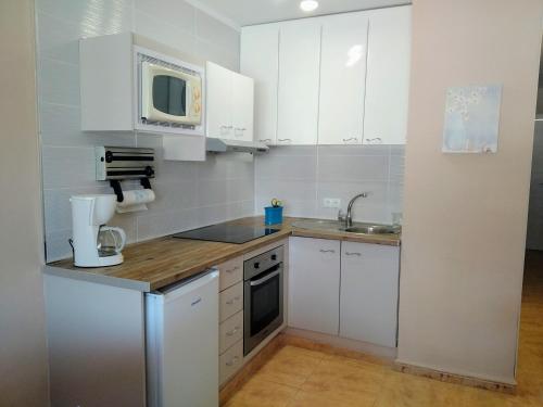 małą kuchnię z białymi szafkami i kuchenką mikrofalową w obiekcie Oasis Marina Apartament w mieście Costa Del Silencio