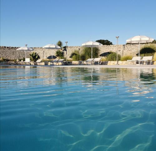 a pool of water with tables and umbrellas at Masseria Del Crocifisso in Polignano a Mare