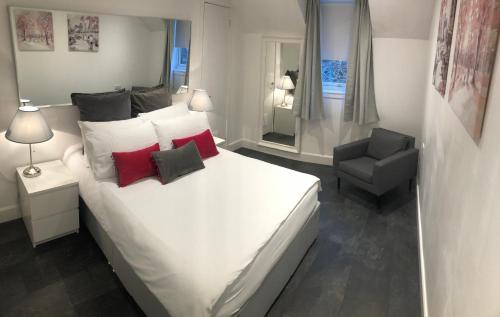 a bedroom with a white bed with red pillows and a chair at L&H APARTMENTS in Inverness