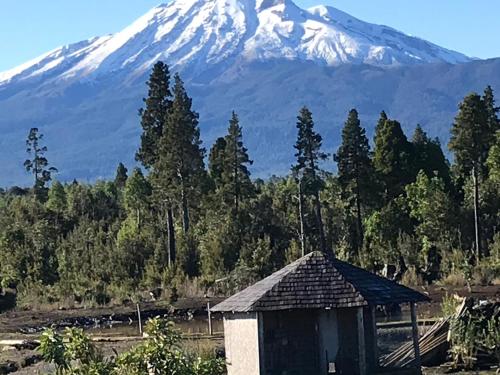 a snow covered mountain in the distance with a hut at Parque la Pajarera in Puerto Varas