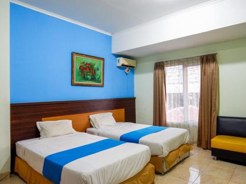 Duas camas num quarto com paredes azuis e uma cadeira em Pineapple Mansion Solo Mitra RedDoorz near RS JIH Solo em Surakarta