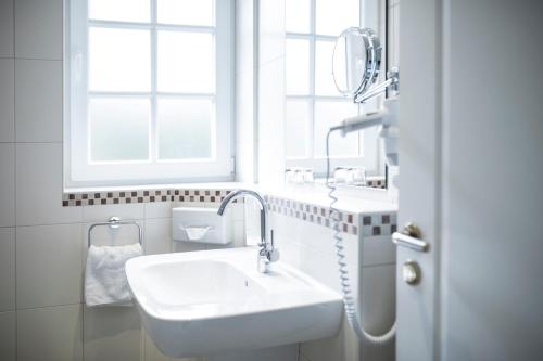 ein weißes Bad mit einem Waschbecken und einem Fenster in der Unterkunft Hotel Wardenburger Hof in Wardenburg