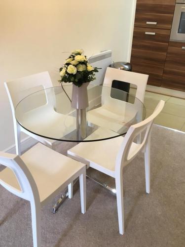 a glass table with two white chairs and a vase with flowers at Blue Sky Apartments @Wallis Square, Farnborough in Farnborough