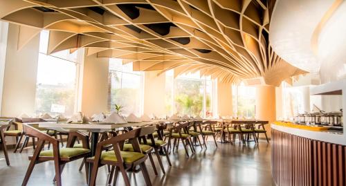 a dining room with tables and chairs under a large ceiling at Rodas An Ecotel Hotel in Mumbai