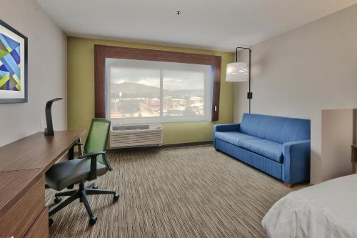 a hotel room with a bed desk and a blue couch at Holiday Inn Express & Suites - Albuquerque East by IHG in Albuquerque