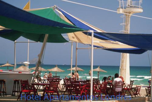 a group of people sitting at a beach under umbrellas at Hotel Apartamentos Londres La Manga in La Manga del Mar Menor