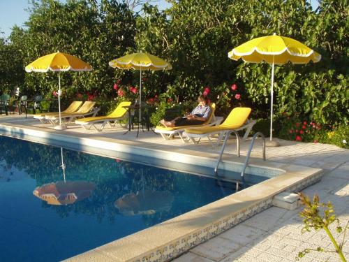 a woman sitting in chairs next to a pool with umbrellas at Monte Da Serralheira Agro Turismo in Évora
