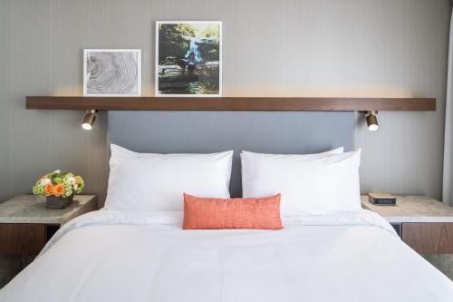 a bed with white sheets and an orange pillow on it at The Domain Hotel in Sunnyvale