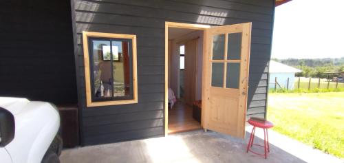 a black house with a door and a stool outside at Domos Eva-Ray in Panguipulli