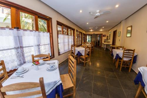 un restaurante con mesas y sillas blancas y ventanas en Pousada Azul Banana - Camburi en Camburi