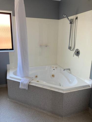 La salle de bains est pourvue d'une baignoire avec douche et d'une fenêtre. dans l'établissement Heritage Highway Motel, à Hokitika