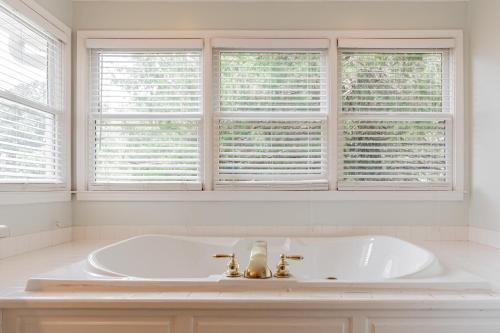 a white bathroom with a tub and two windows at Fire Pit * Pool * Hot Tub * Fishing Pond w/ Jon Boat in Easley