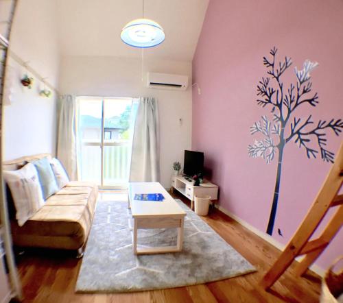 una sala de estar con sofá y un árbol pintado en la pared en グレース大磯, en Oiso