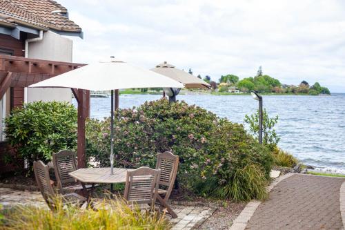 a table with chairs and an umbrella next to the water at Cascades Lakefront Motel in Taupo