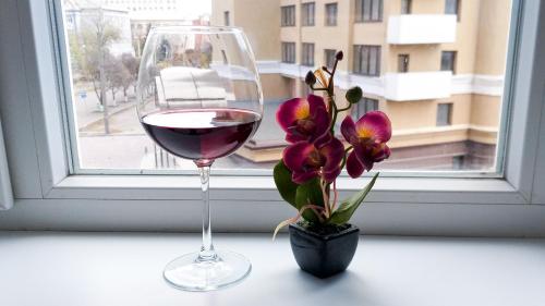 a glass of wine and a vase with flowers on a window at Белая студия на Южном вокзале in Kharkiv