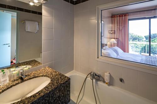 a bathroom with a tub and a sink and a window at Hotel Provençal in Hyères