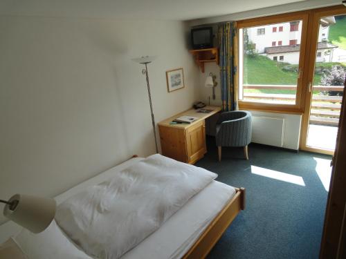 a bedroom with a bed and a desk and a window at Hotel Alpina Parpan in Parpan