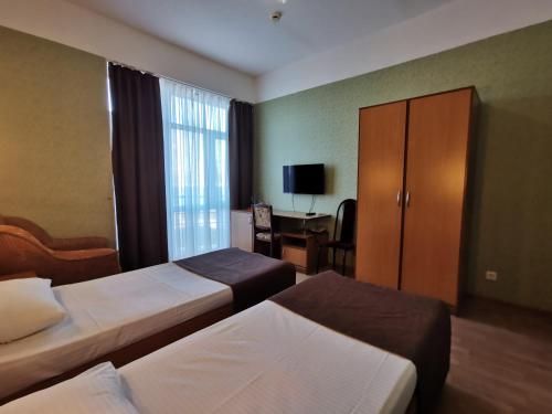 アナパにあるAtlantida Hotelのベッド2台、キャビネット、デスクが備わるホテルルームです。