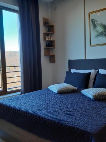 a bedroom with a blue bed with a large window at Dream Milmari L12 Apartman in Kopaonik