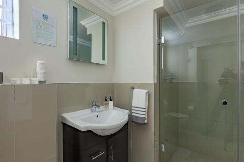 a bathroom with a sink and a glass shower at The Sir David Boutique Guest House in Bloubergstrand