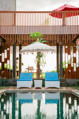 due sedie e un ombrellone accanto a una piscina di The Ume a Canggu