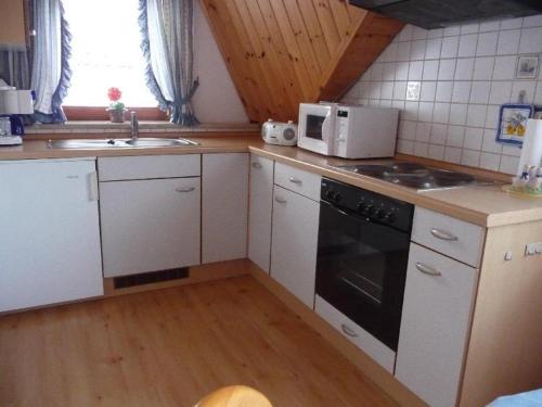 Una cocina con gabinetes blancos, estufa y microondas. en Ferienwohnung-Nr-1, en Vöhrenbach