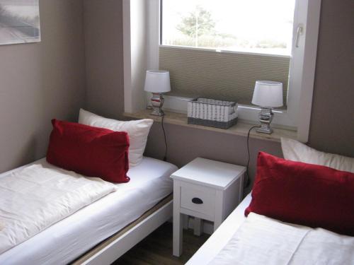 Cette chambre comprend 2 lits avec des oreillers rouges et une fenêtre. dans l'établissement Haus-Quisisana-App-6, à Westerland