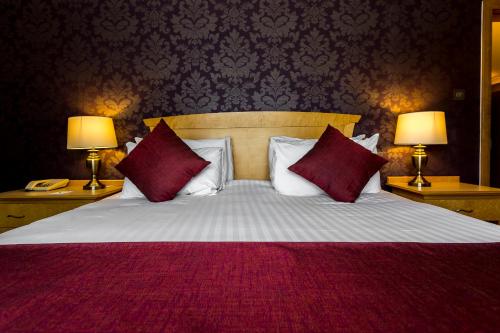 a bedroom with a bed with red pillows and two lamps at Hellidon Lakes Hotel in Daventry