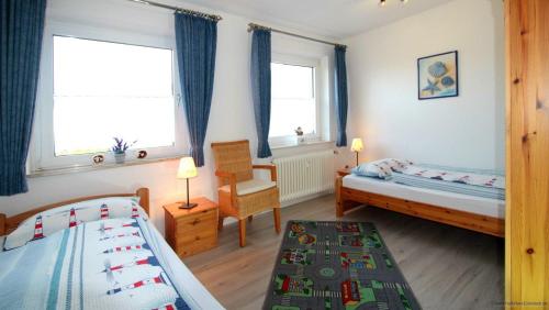 een slaapkamer met 2 bedden, een stoel en 2 ramen bij Haus-am-Boehler-Strand-Wohnung-2 in Süderhöft