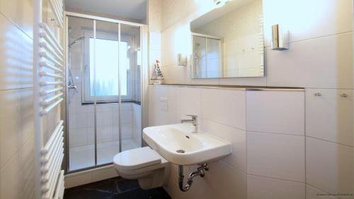 een witte badkamer met een wastafel en een douche bij Haus-am-Boehler-Strand-Wohnung-2 in Süderhöft
