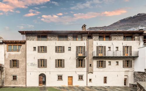 un antiguo edificio blanco con ventanas y una montaña en Curt di Clement Eco Mobility Hotel, en Tirano