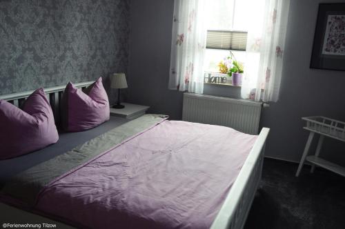ein Schlafzimmer mit einem Bett mit lila Kissen und einem Fenster in der Unterkunft Ferienwohnung "  An der Koppel " in Mölln-Medow