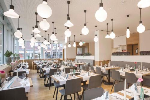 un restaurante con mesas blancas, sillas y luces en Stadthotel Münster, en Münster