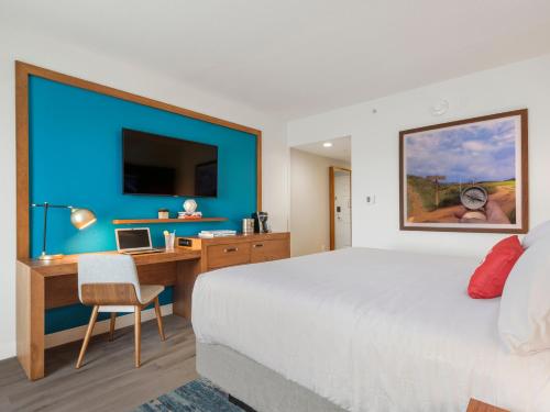 a hotel room with a bed, desk and a painting on the wall at Compass Hotel by Margaritaville Anna Maria Sound in Bradenton