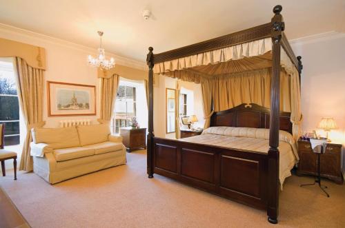 a bedroom with a canopy bed and a chair at Orton Hall Hotel & Spa in Peterborough