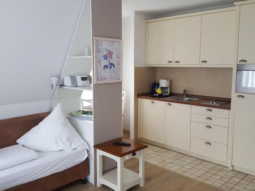 una cocina con armarios blancos, una cama y una mesa en Sylter-Besserburg-App-9, en Westerland
