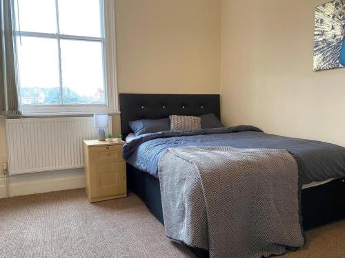 a bedroom with a bed and a nightstand and two windows at Spacious Victorian Studio Flat in Doncaster
