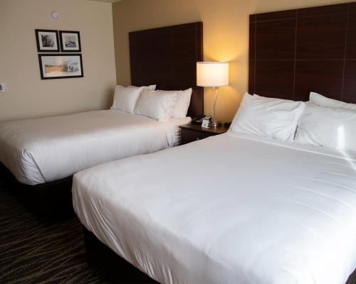 two beds in a hotel room with white sheets at Cobblestone Hotel & Suites - Two Rivers in Two Rivers
