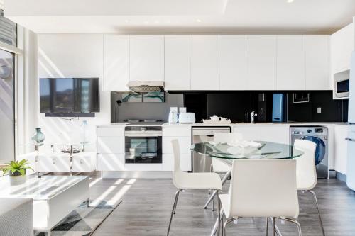 a white kitchen with a glass table and white chairs at Backup-Powered Trendy City Sanctuary in Cape Town